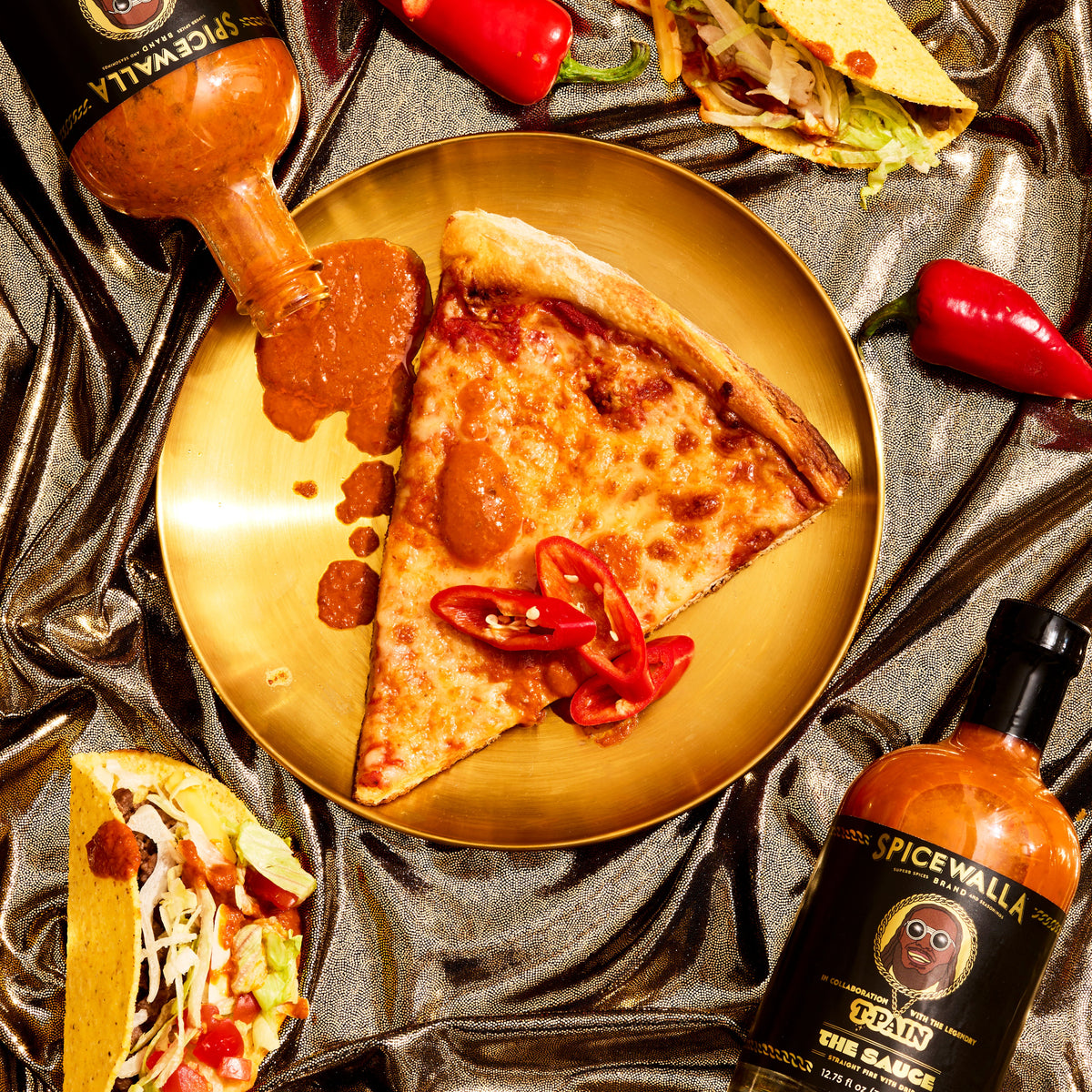Spicewalla hot sauce bottle with orange glass, next to pizza on a pan.