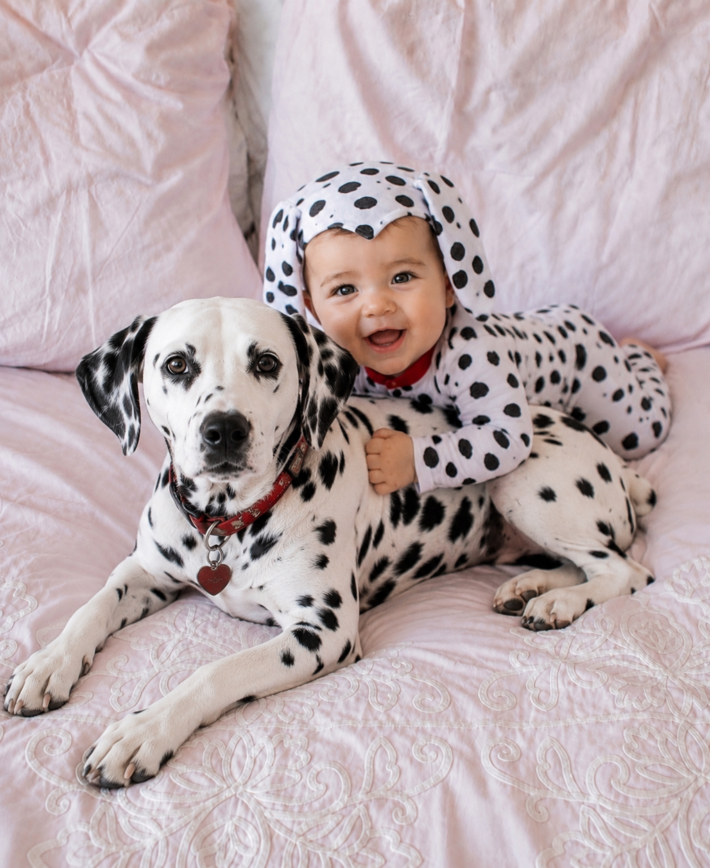 Baby wearing hooded Dalmatian costume with black spots and red collar trim, lying down