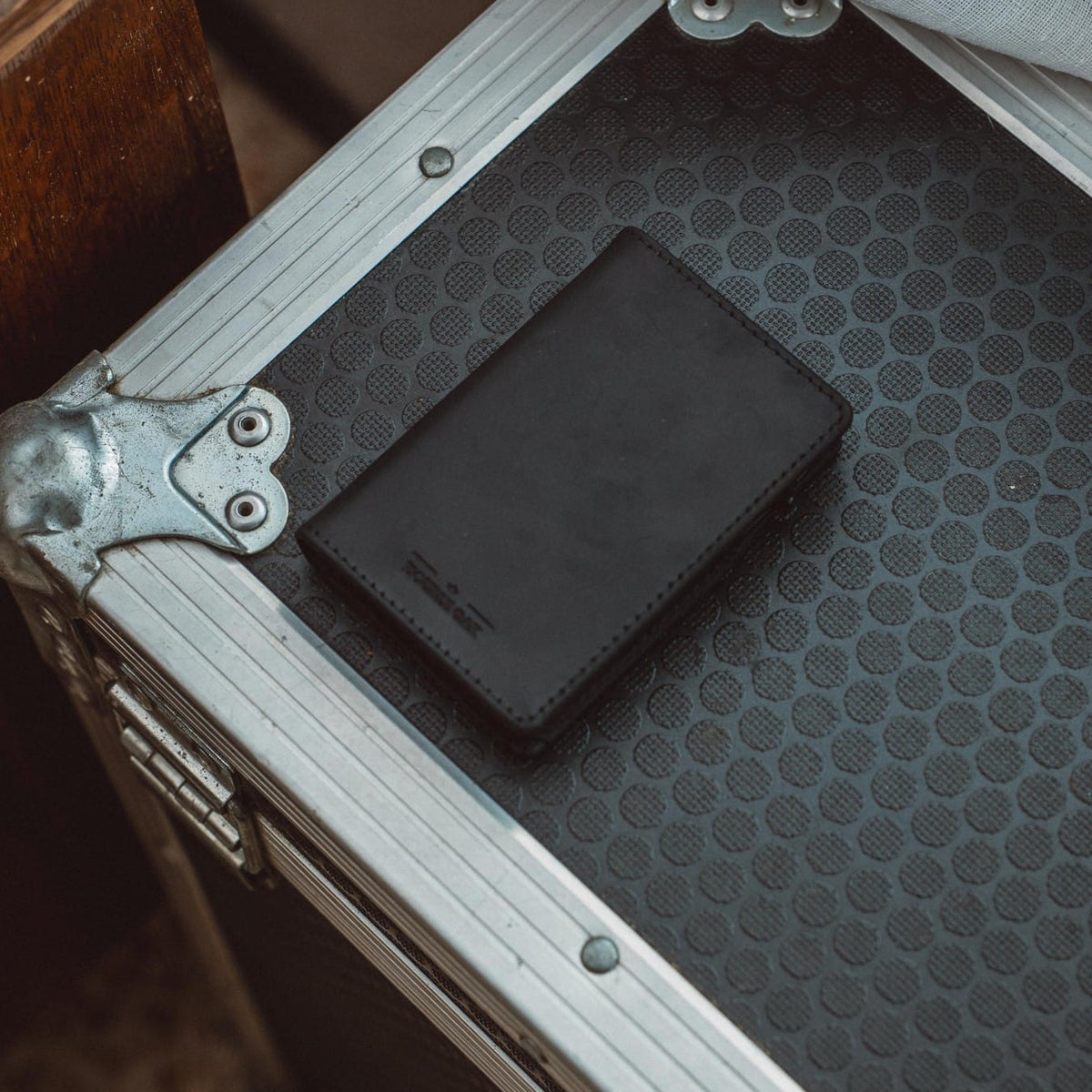Bifold wallet, dark leather, on patterned gray suitcase with embossed logo.