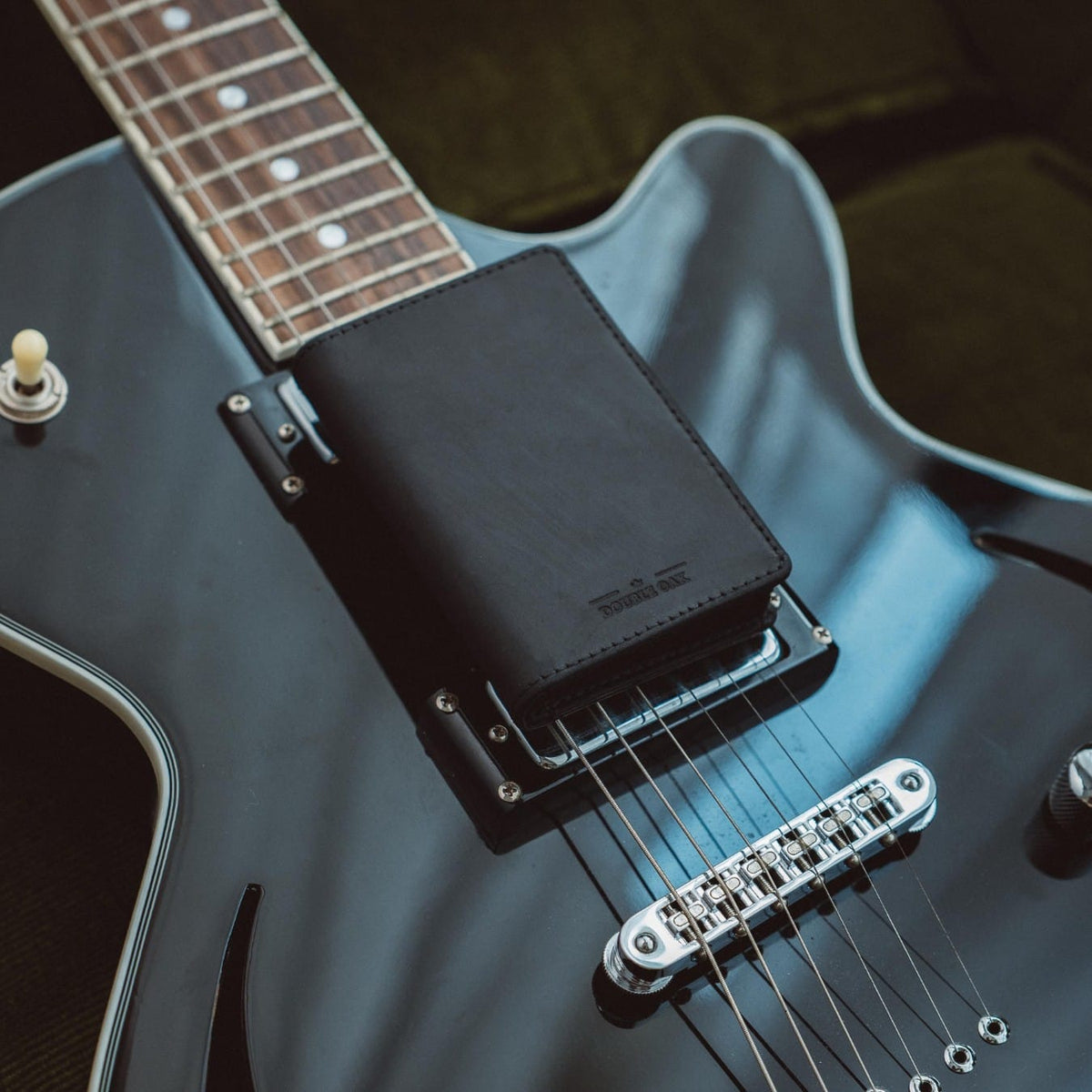 Bifold wallet, black leather, placed on a blue electric guitar body near the bridge.