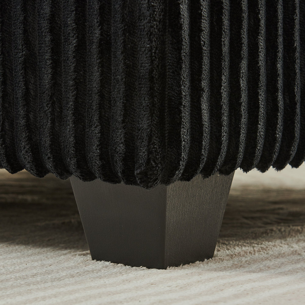 Black corduroy upholstery close-up on sofa arm cushion with dark tapered legs