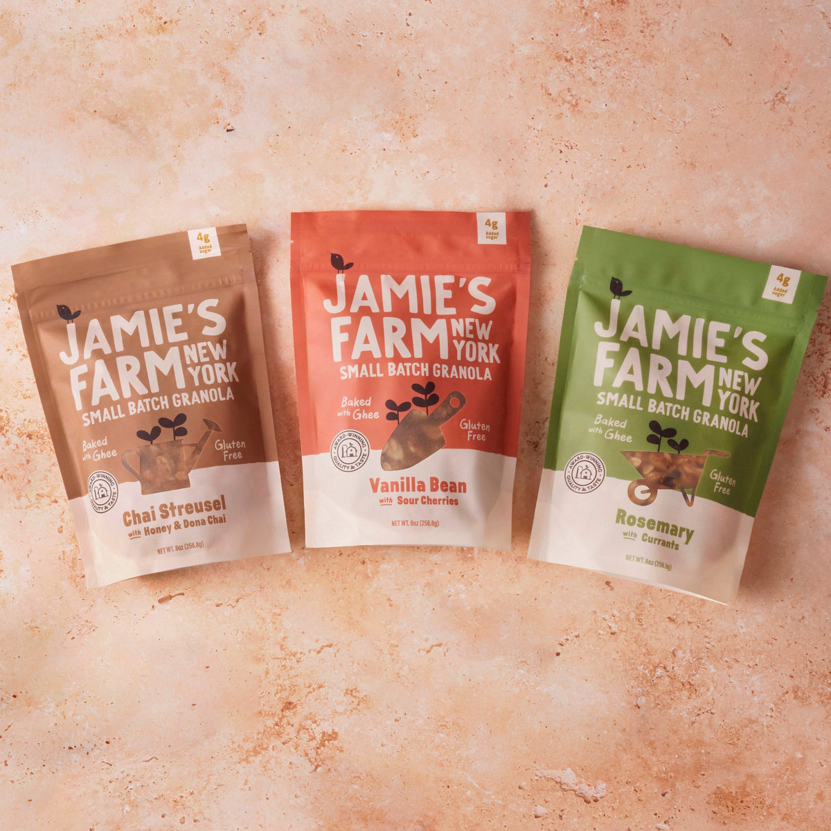 Three small-batch granola pouches in brown, pink, and green on a surface