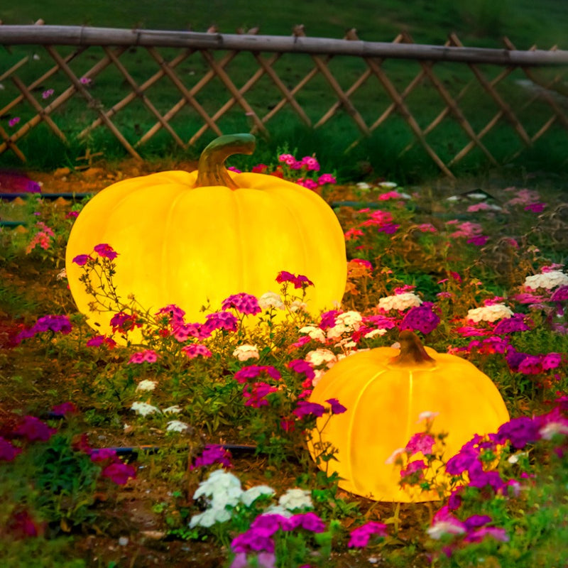 Glowing golden yellow pumpkin LED lights with two sizes, outdoors among flowers