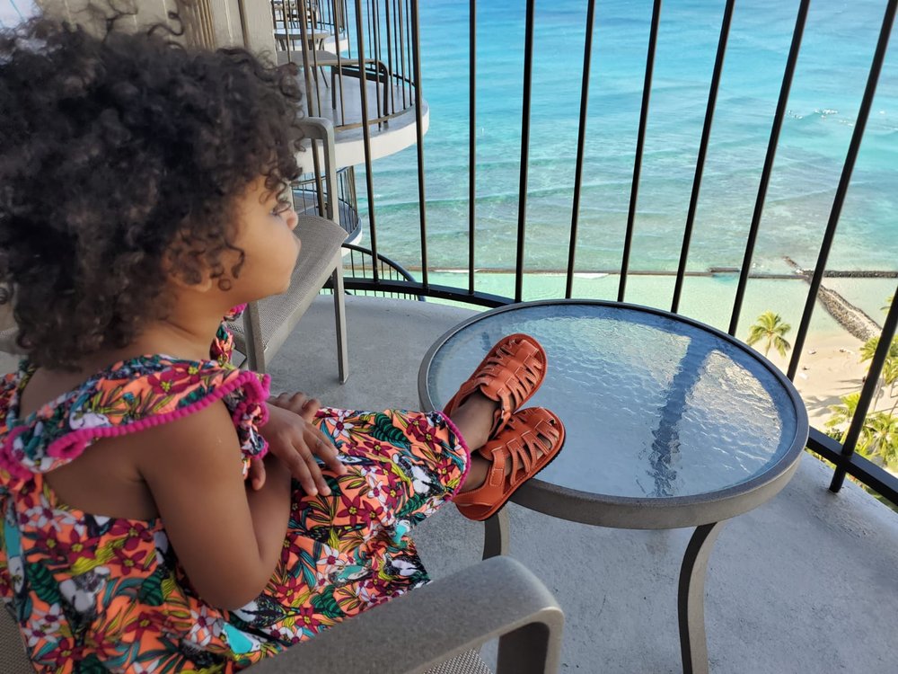 Orange kids sandals on a child’s feet near a railing, open-toe with velcro straps