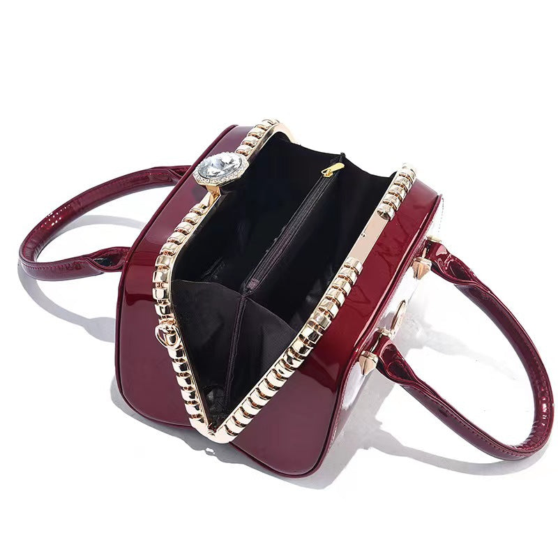 Wine red glossy handbag with open top, top handles, and rhinestone chain trim