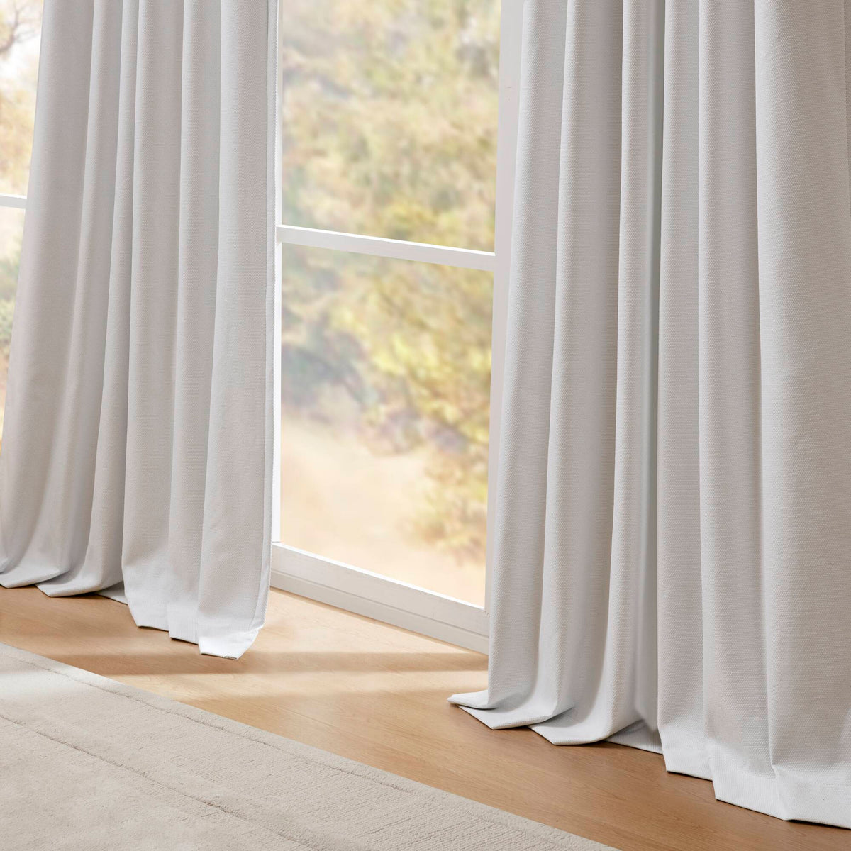 White blackout curtain panels covering a window, full-length flowing drape