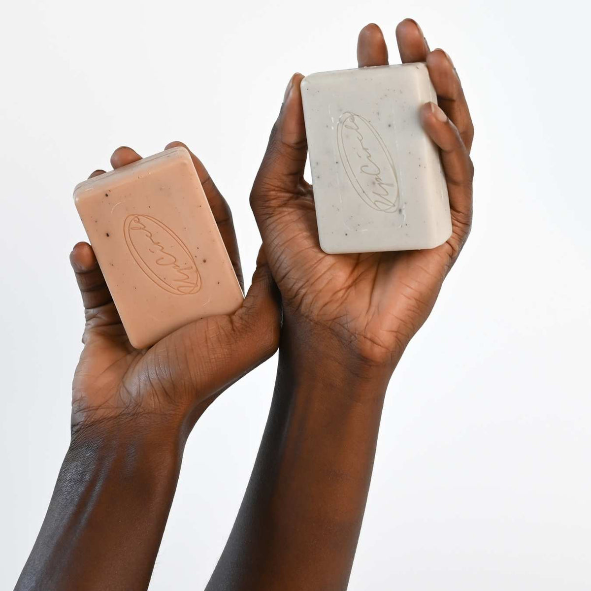 Hands holding two rectangular cleansing soap bars, beige and cream, with UpCircle logo