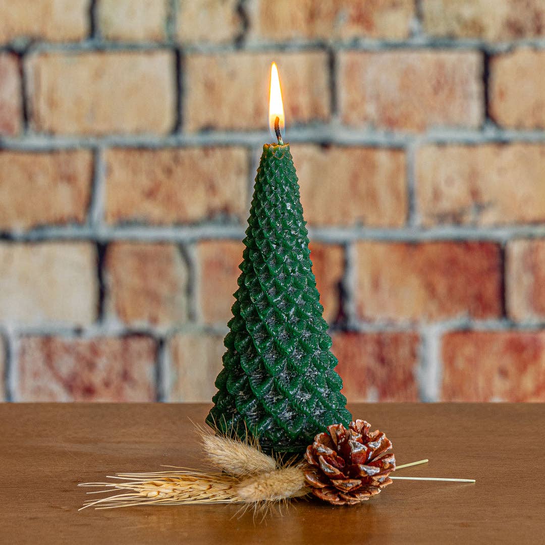 Green tree-shaped candle with flame, pinecone and straw on tabletop