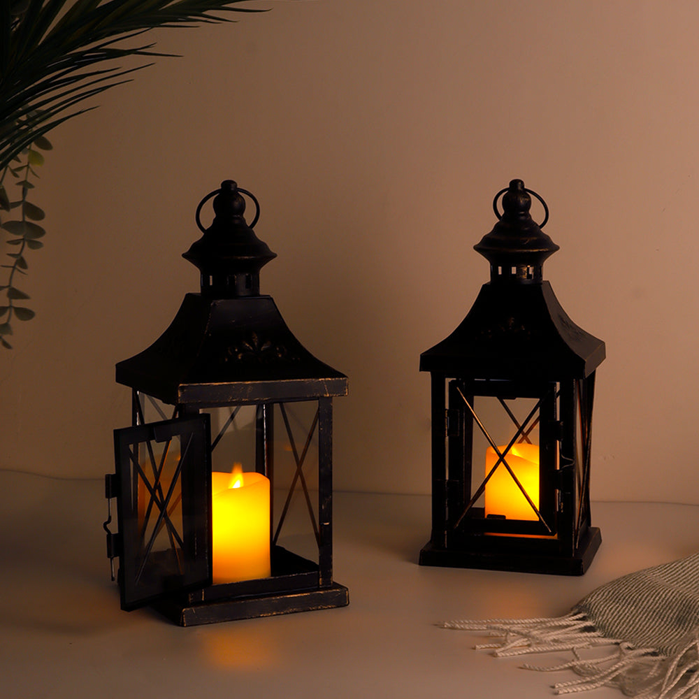 Two black metal hanging candle lanterns with lit candles inside and cross-braced frames