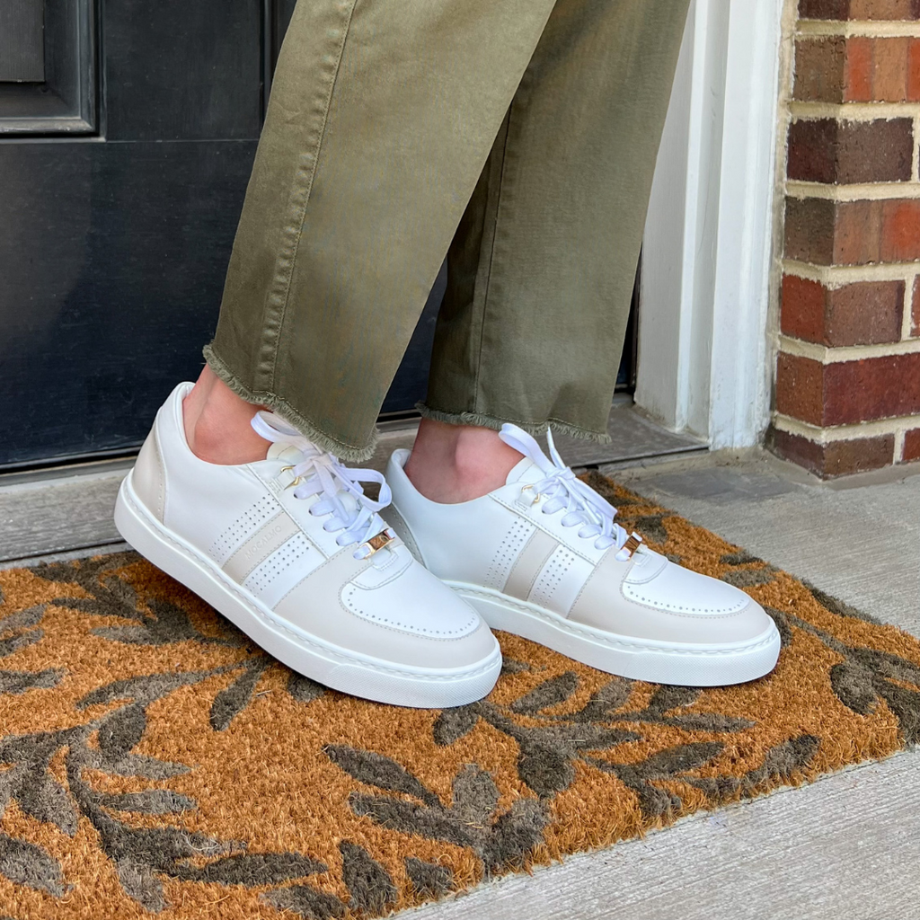 Women’s ivory sneakers with gray accents, worn with olive pants on a front doormat