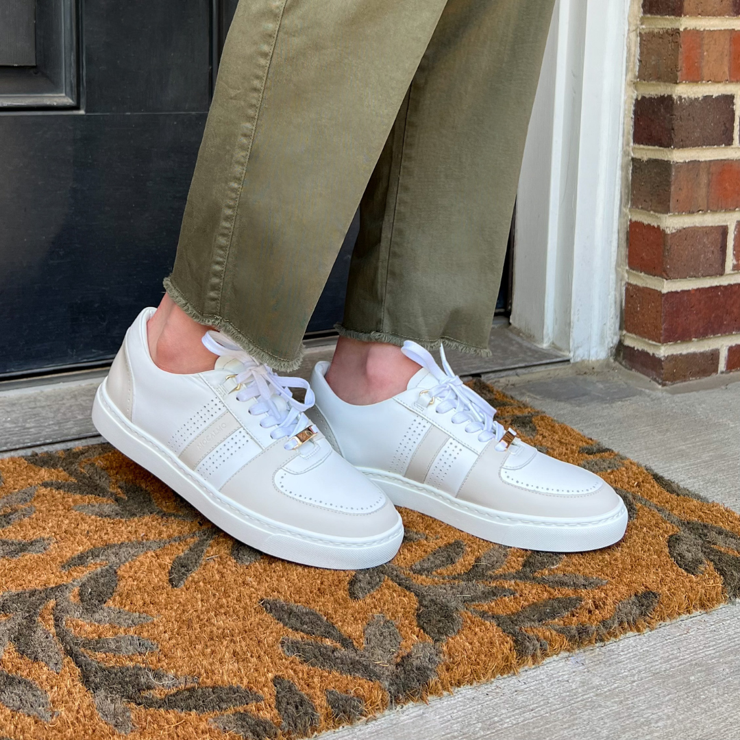 Women’s ivory sneakers with gray accents, worn with olive pants on a front doormat