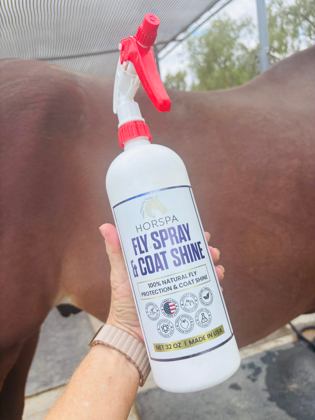 Horse fly spray and coat shine bottle with sprayer, held near brown horse