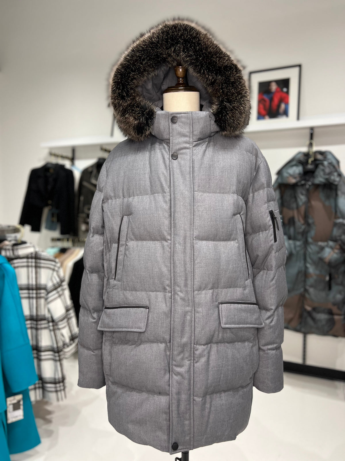 Grey long puffer coat with faux fur hood trim, center front zipper, and flap pockets