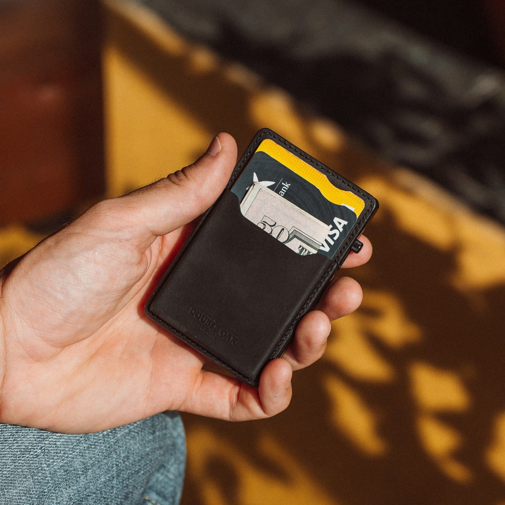 Black leather cardholder wallet with cards and yellow trim, held in a hand.