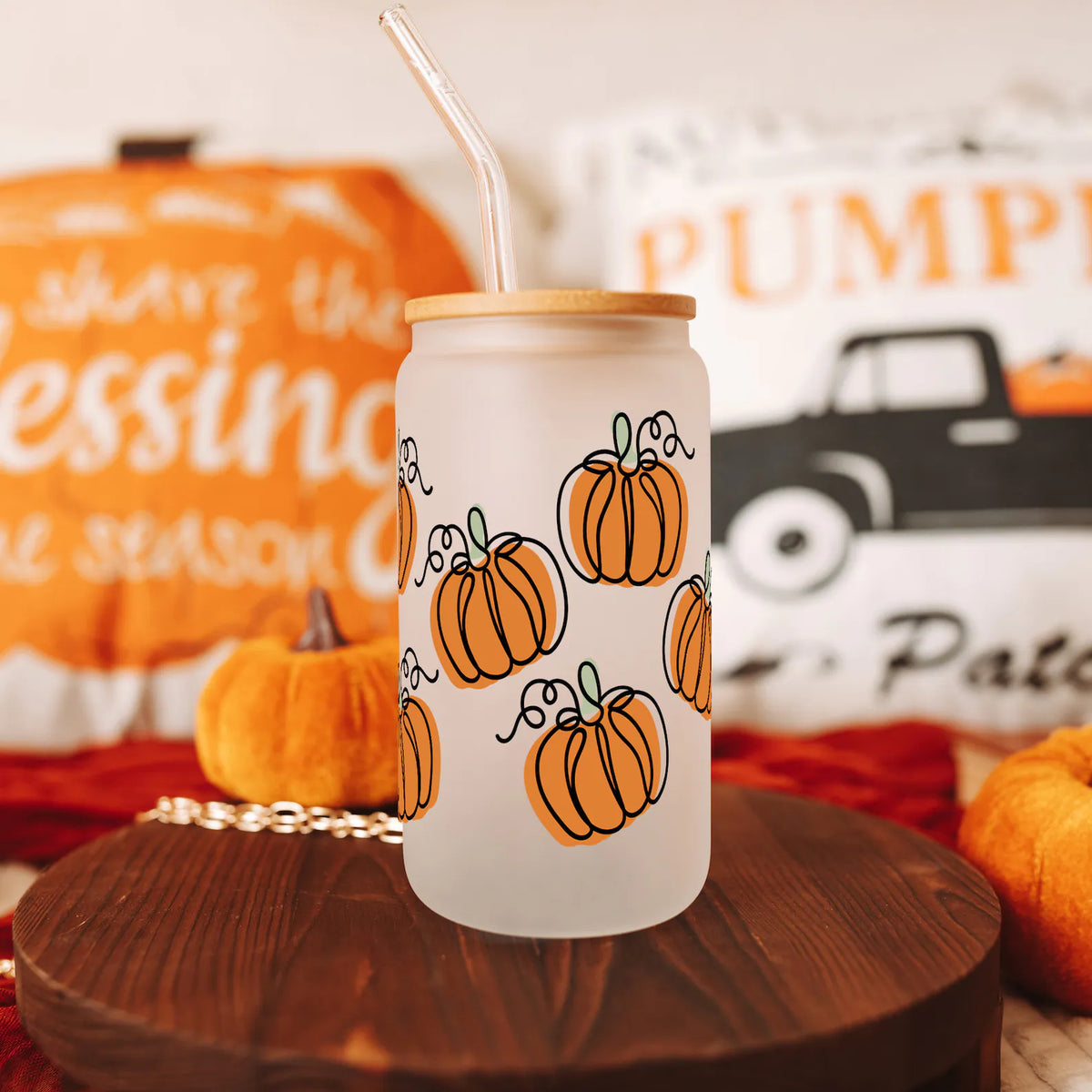 Frosted glass tumbler with orange pumpkin print, bamboo lid and straw on table