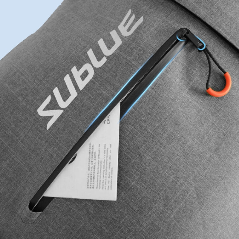 Gray waterproof backpack flap with blue-trim zipper and orange carabiner key loop