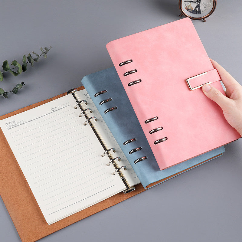A5 pink loose-leaf notebook with metal rings, open pages, and buckle strap