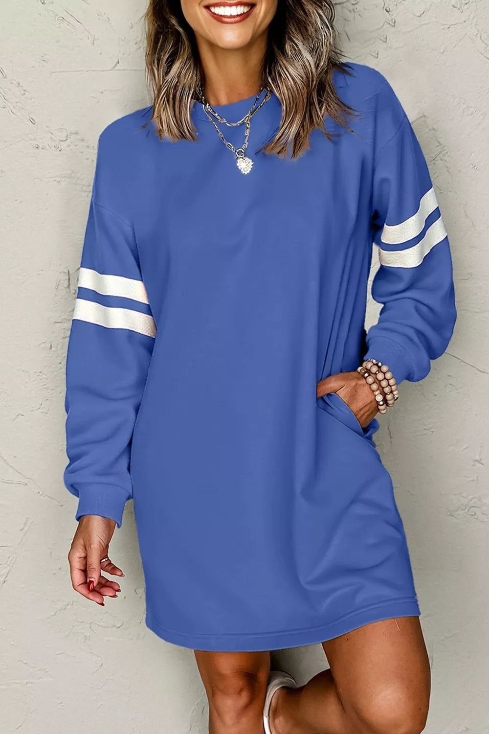 Dusty blue long-sleeve sweatshirt dress with white striped sleeve details and curved hem.