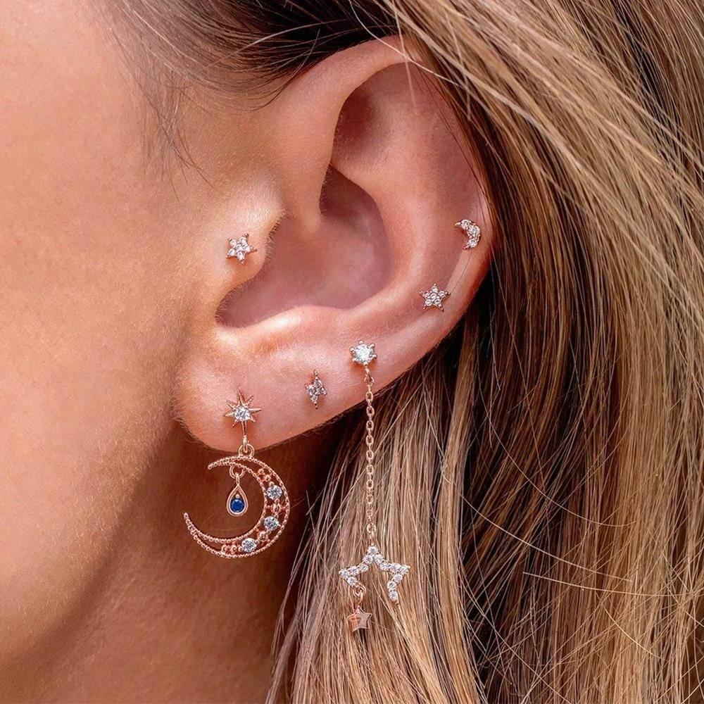 Gold stacked star and crescent earrings with zirconia studs and dangling charm on ear.