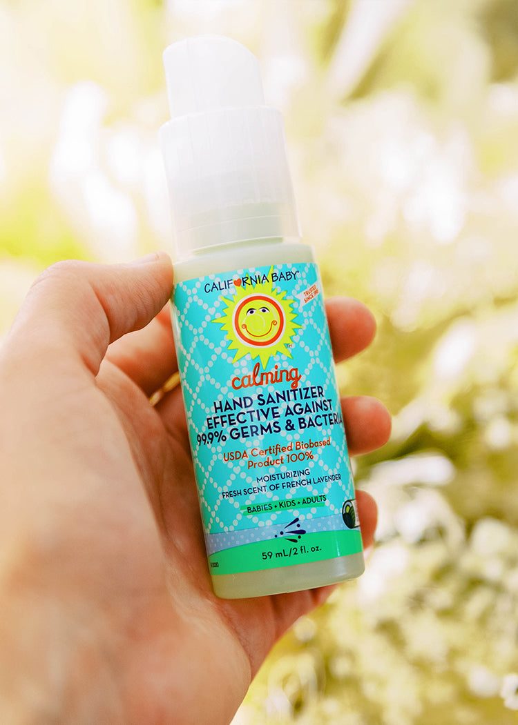 Hand holding a small hand sanitizer bottle with teal label, 59 mL.