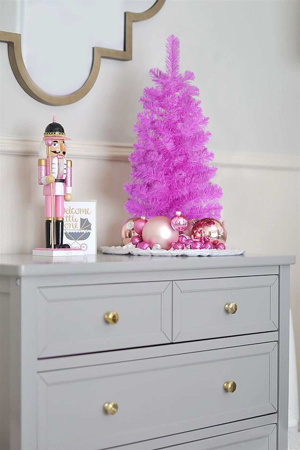 Pink tabletop Christmas tree on stand with ornaments on a sideboard