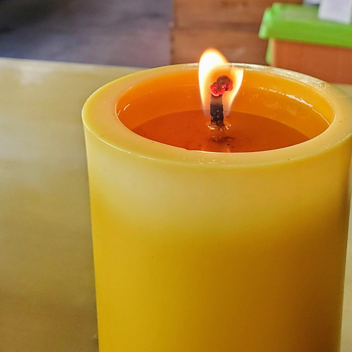Burning yellow beeswax pillar candle with glowing flame and visible wick