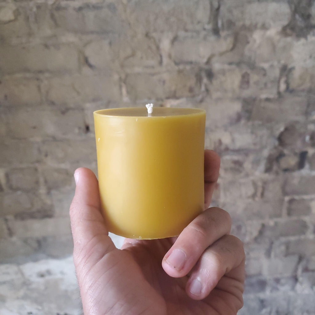Hand holding a yellow beeswax pillar candle with exposed wick, front view