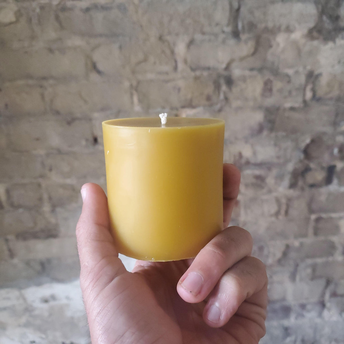 Hand holding a yellow beeswax pillar candle with exposed wick, front view
