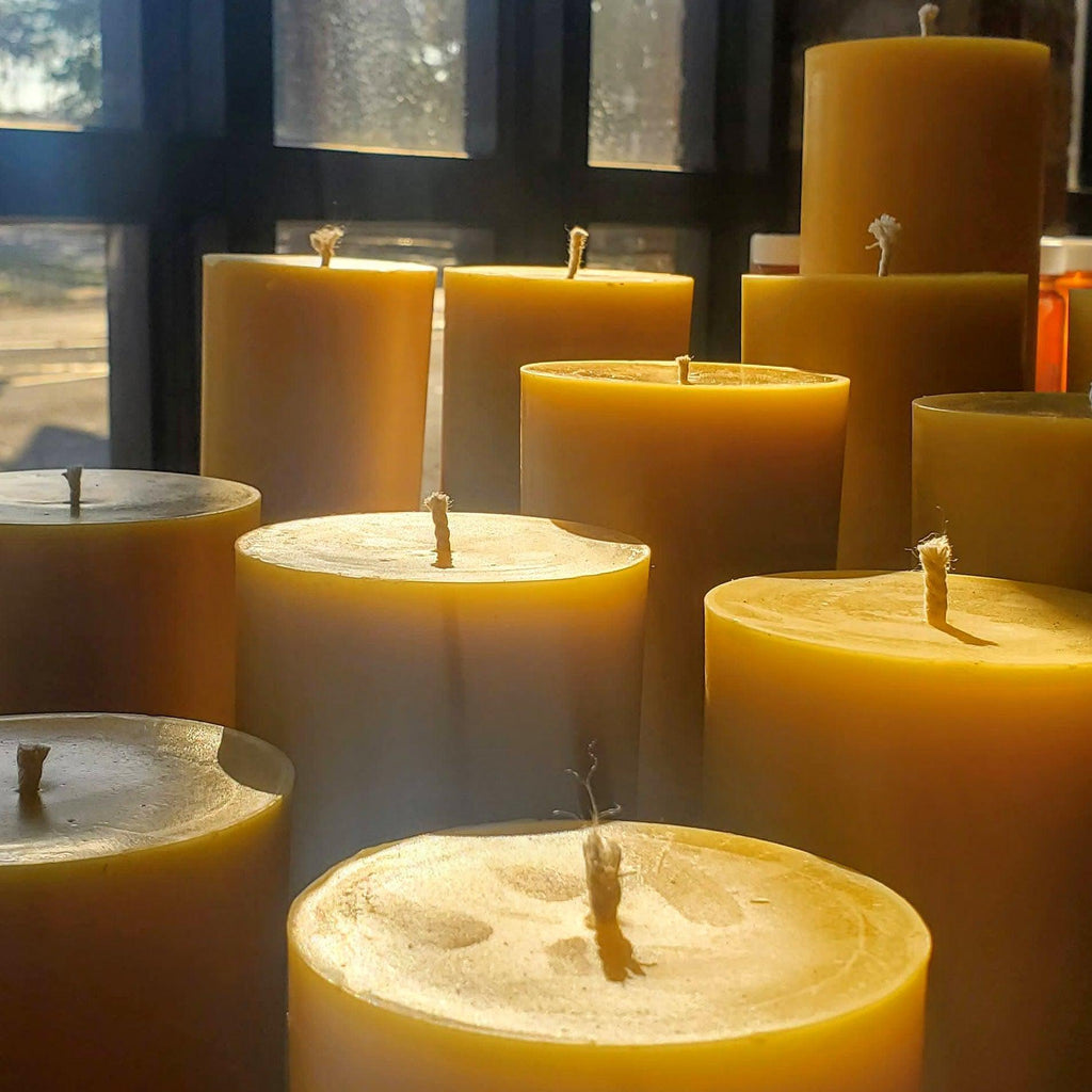 Multiple tall yellow beeswax pillar candles with centered wicks, lit and unlit