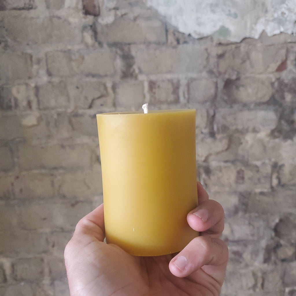Hand holding a yellow beeswax pillar candle with exposed wick, front view