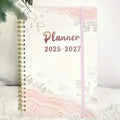 Spiral-bound monthly planner with pastel floral cover and “Planner 2025–2027” title