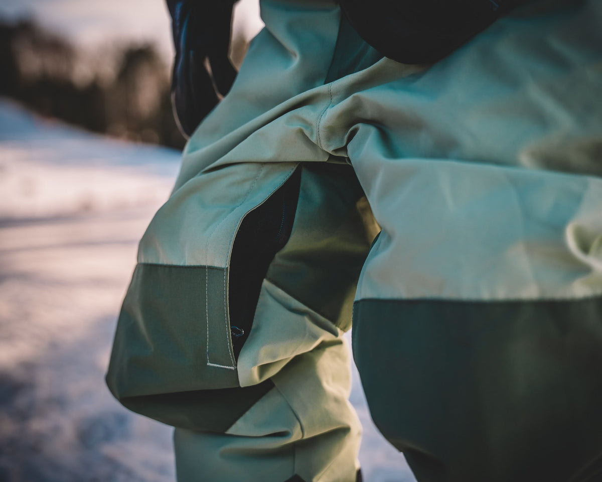 Waterproof snowsuit jacket close-up in dark green with light side panel and seam detail
