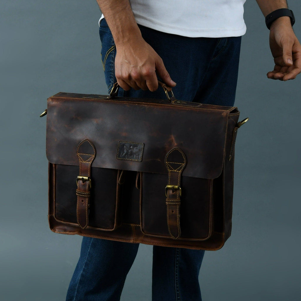 Brown leather briefcase held by a person, with flap front pockets and shoulder strap.