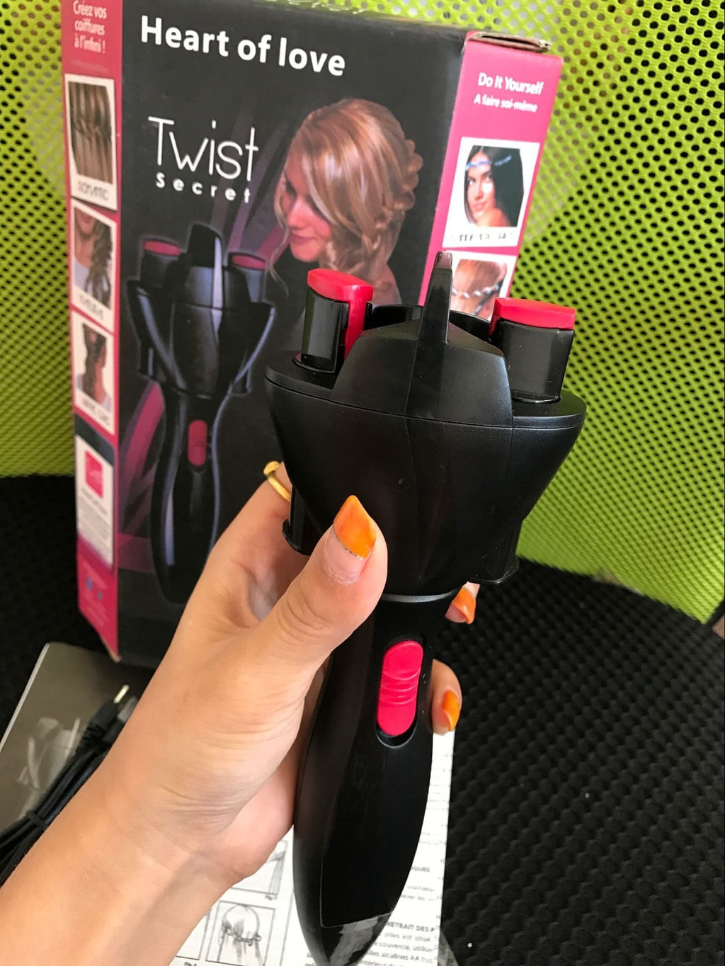 Black hair braider and twister tool held in hand, with red switches and orange light