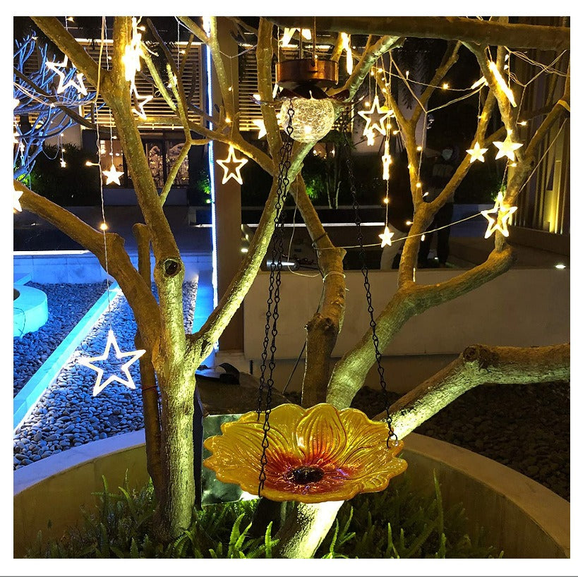 Hanging sunflower bird feeder with glowing clear glass bulb and metal chain in yard