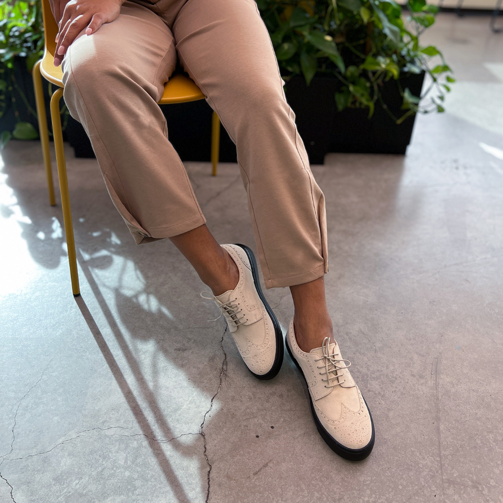 Ivory lace-up oxford shoes with black soles, worn with tan ankle-length pants