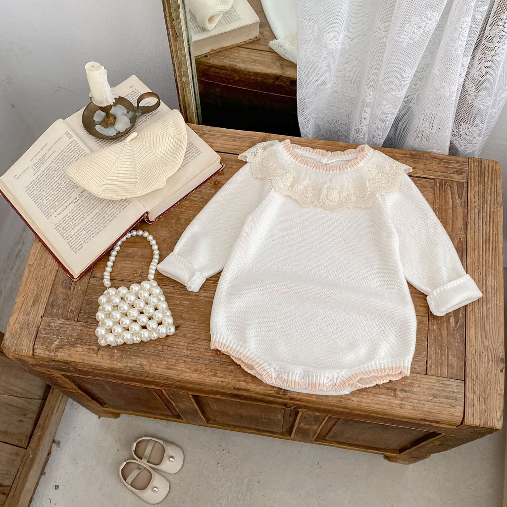 Off-white baby romper with lace collar, long sleeves, and frayed knit hem trim