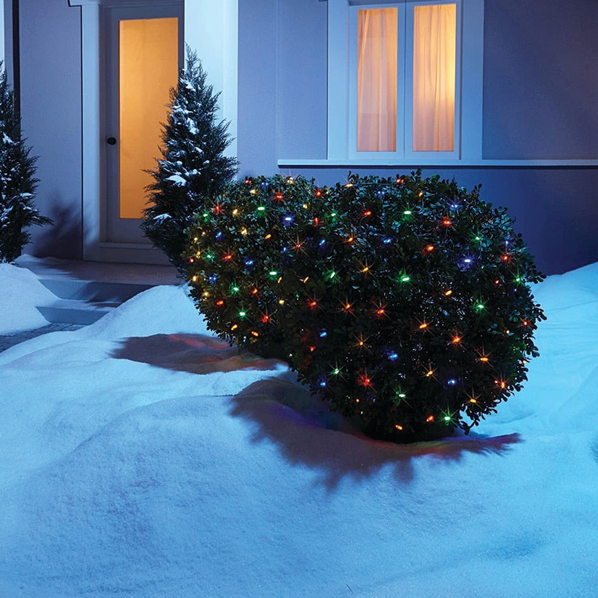 Multicolor LED net lights on a snow-covered shrub at dusk