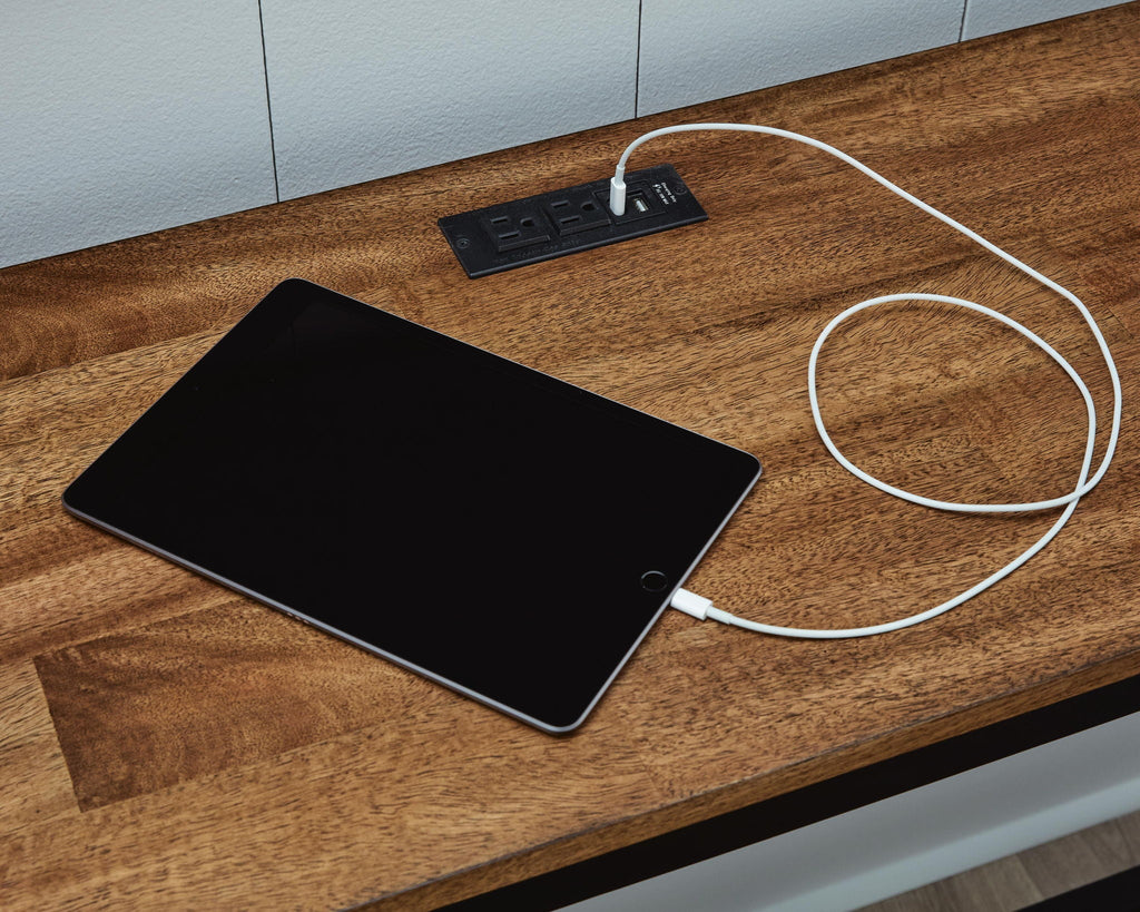 Brown wood countertop with black power strip and white charging cord