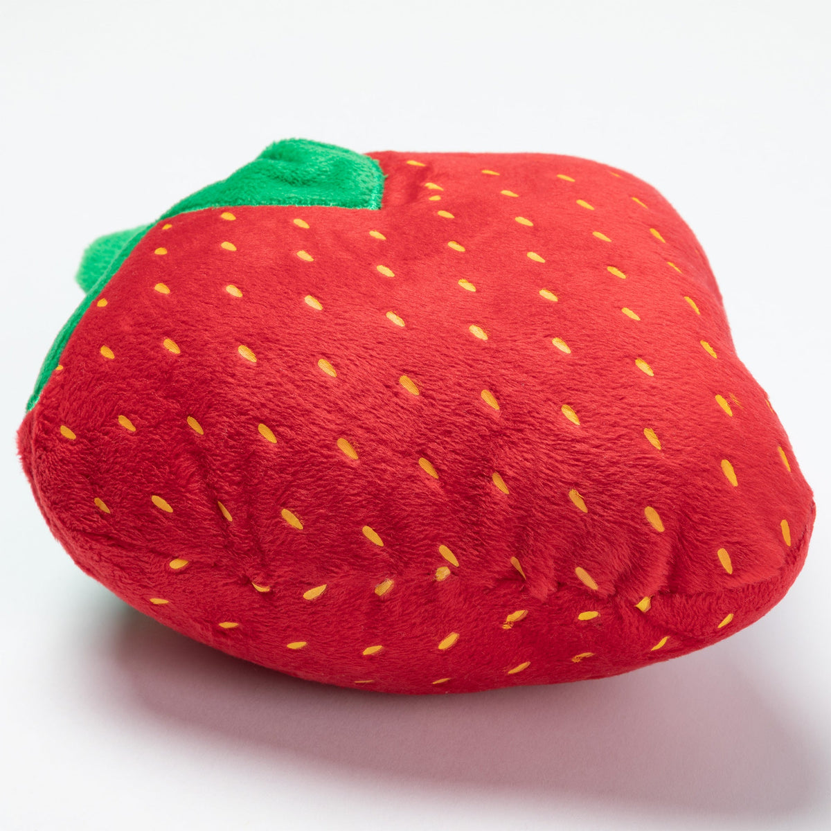 Plush strawberry dog toy close-up, red fabric with yellow seed dots and green leaves.