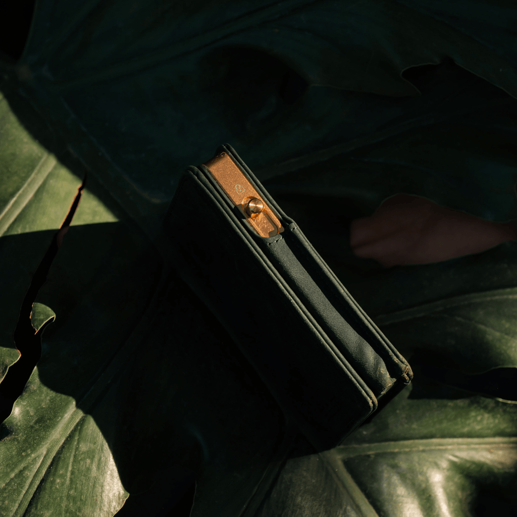 Dark green bifold wallet open, showing card slots and gold hardware.