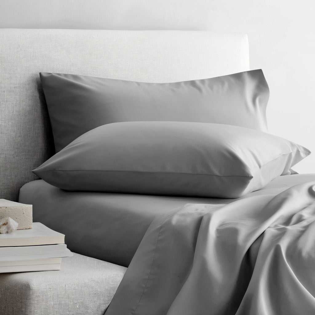 Gray sateen sheet set on bed with two pillowcases and neatly draped sheet