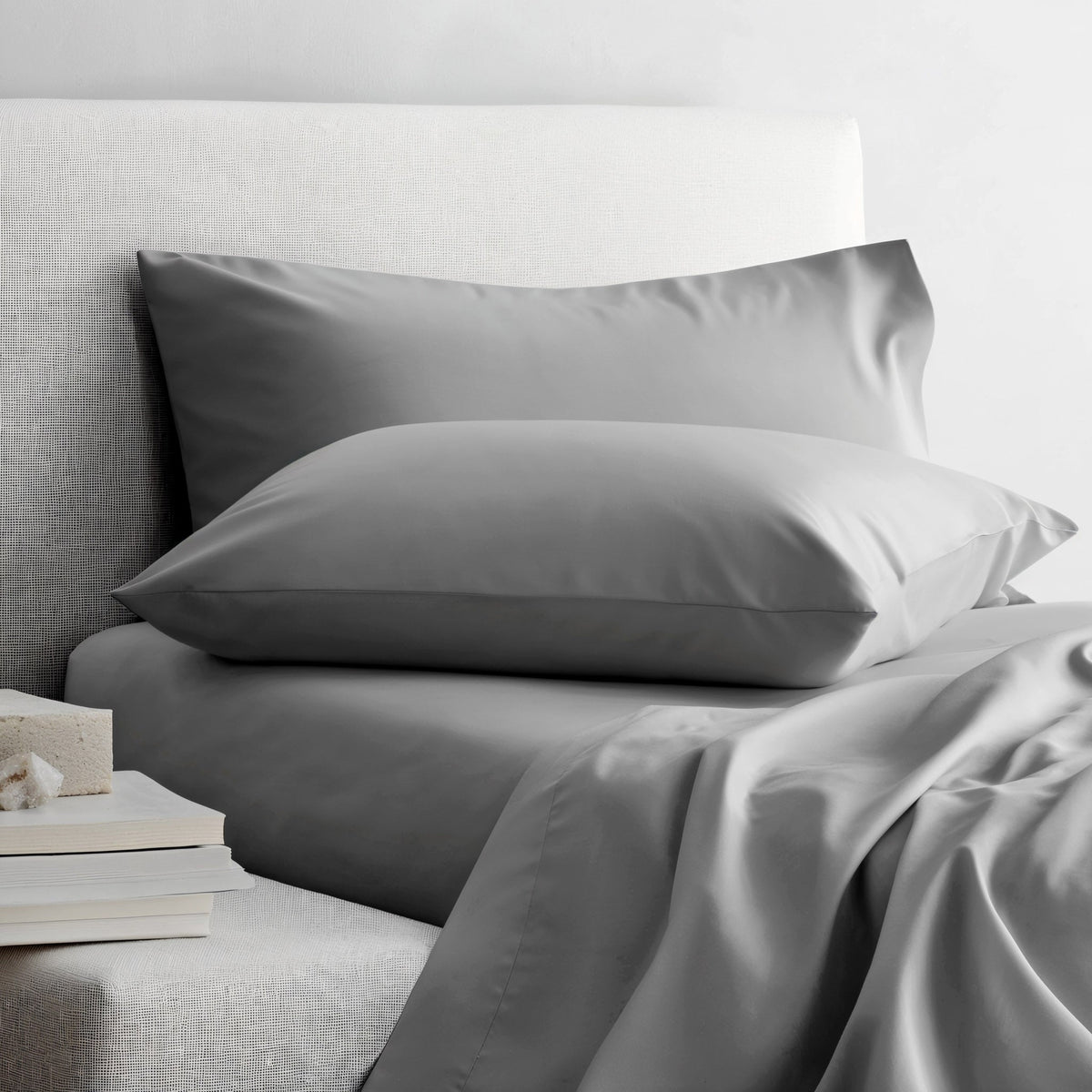 Gray sateen sheet set on bed with two pillowcases and neatly draped sheet