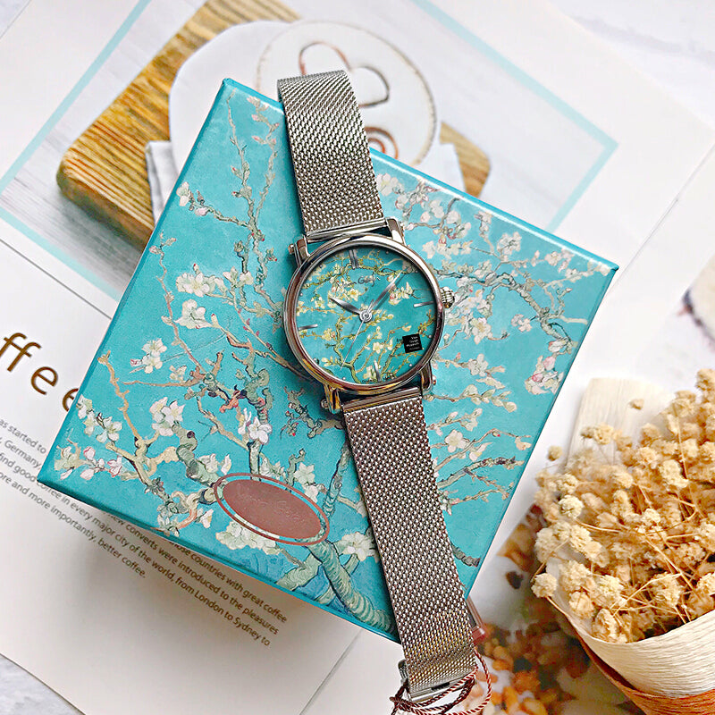 Women's quartz watch with teal floral dial and silver mesh strap on top of cards.
