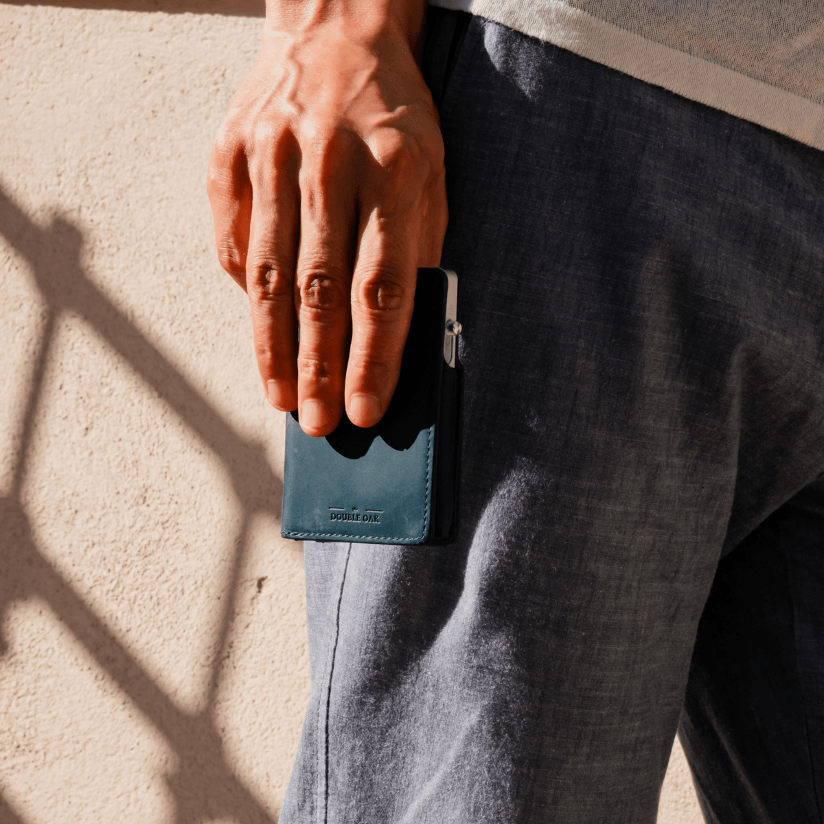 Teal blue leather bifold wallet with silver clasp, held by a person.