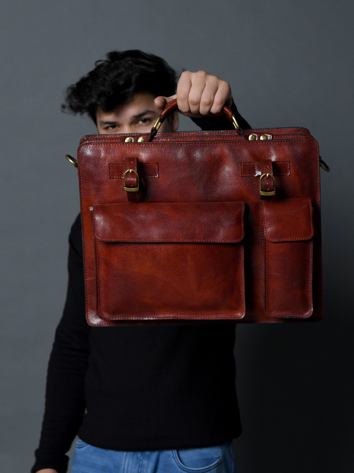 Tan leather briefcase held by handle with front flap and two buckle-locks.