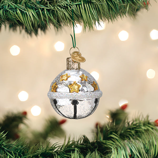 Silver jingle bell ornament hanging from a tree, with glitter and gold star details.
