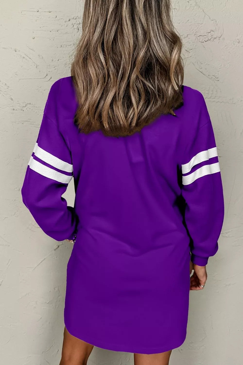 Back view of purple sweatshirt dress with white striped sleeves and relaxed silhouette.