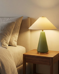 Olive green table lamp with white fabric shade and brass base on a nightstand