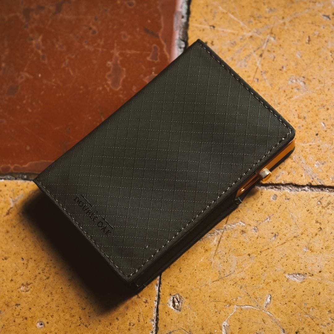 Dark gray fabric bifold wallet on textured surface with gold snap